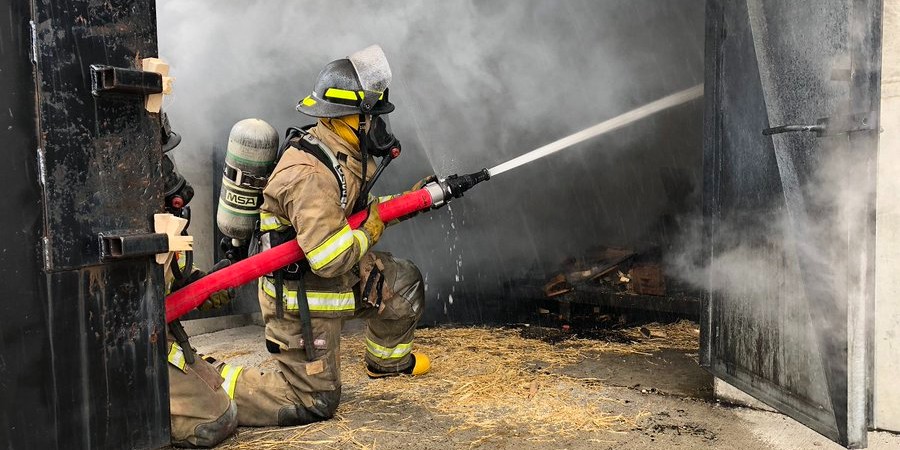 A firefighter in full gear pulling a hose during training.